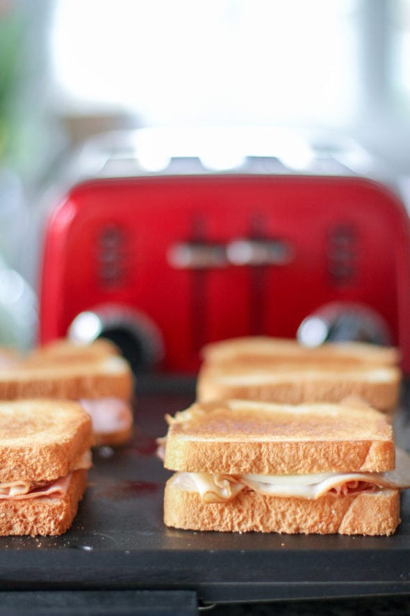 Grilled sandwiches on a griddle with a red toaster in the background.