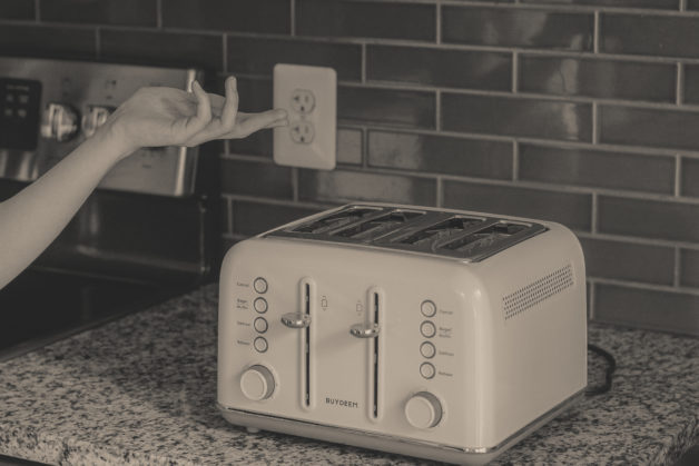 Buydeem Toaster on a countertop, black and white photo.