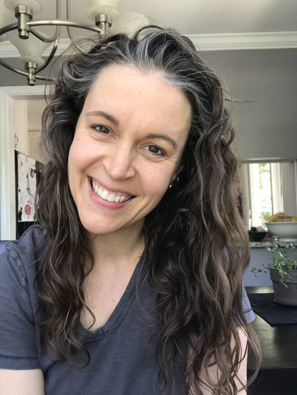 Kristen with wavy hair, smiling at the camera, wearing a gray shirt.