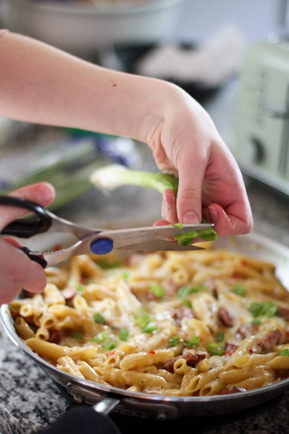 Sonia cutting green onions into a skillet of pasta.