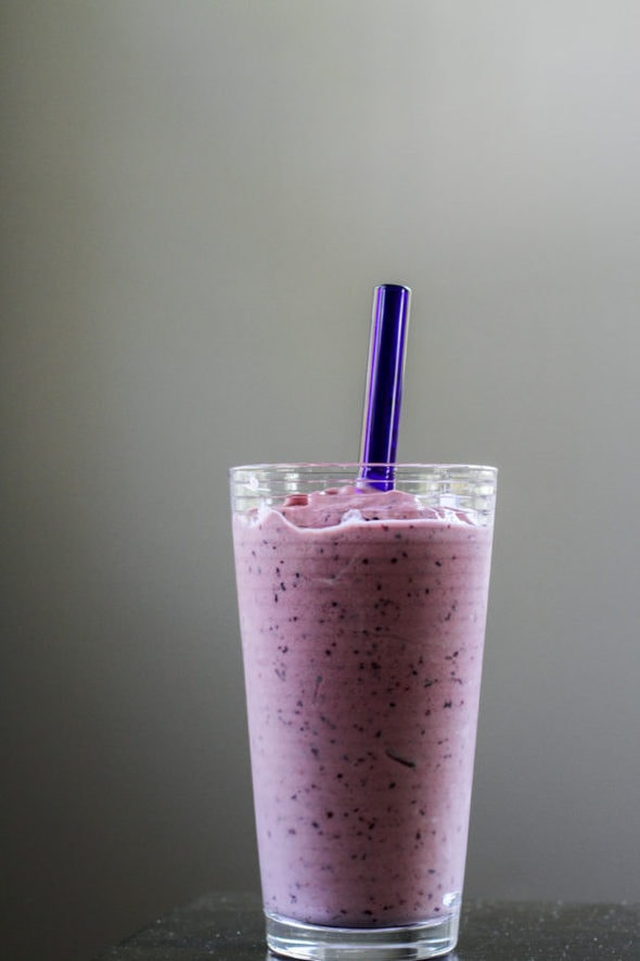Purple blueberry-peach smoothie in a glass with a blue glass straw.