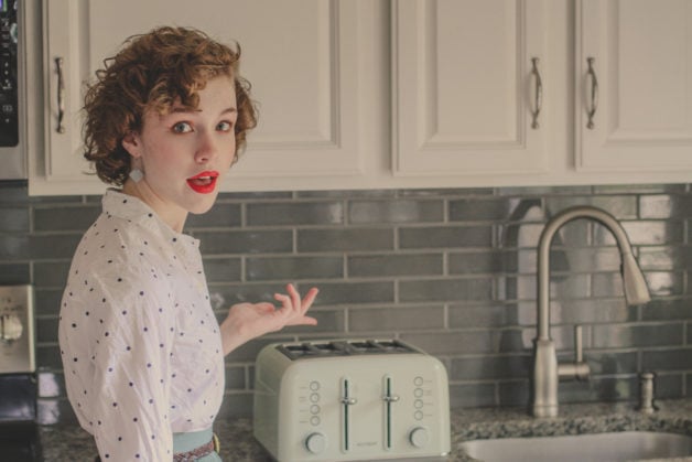 Sonia, looking retro, gesturing toward a green toaster.