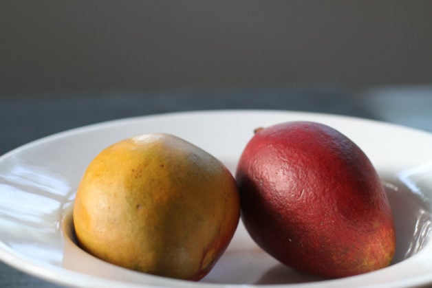 A red mango and yellow mango in a white bowl.