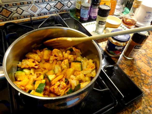 Vegetables being cooked in a pot, with a wooden spoon.