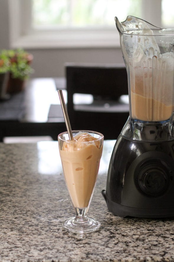 A peach smoothie in a soda fountain glass, next to a Vitamix One blender.