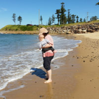 Emma with her child, standing on a beach.