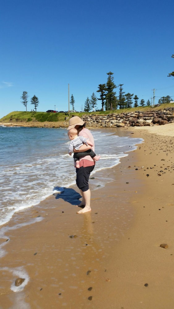 Emma with her child, standing on a beach.