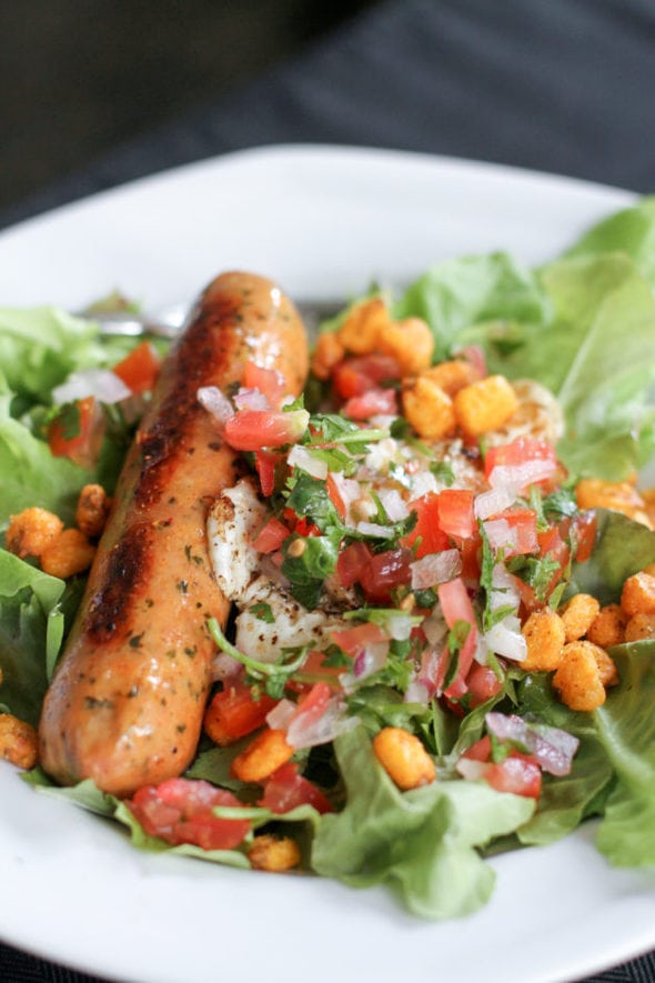 A green salad topped with a sausage, an egg, and pico de gallo.