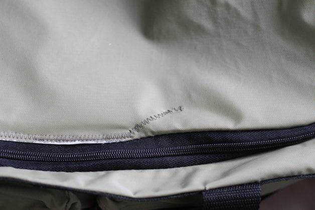 A zig-zagged rip repair on a taupe duffel bag.