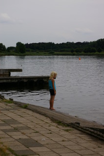 A blonde girl standing at a pond's edge.