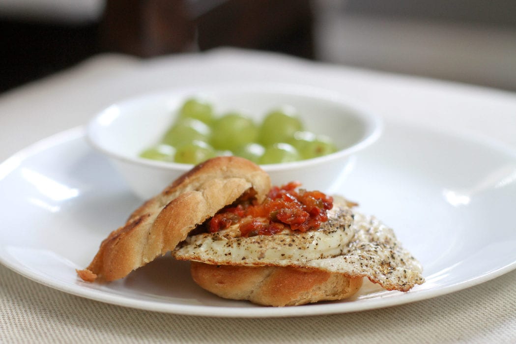 A fried egg sandwich with a bowl of grapes.