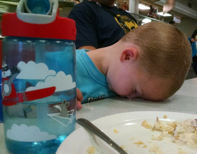 A little boy asleep with his head on a table.