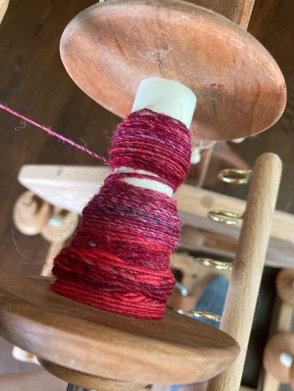 A spinning wheel with pink yarn on it.