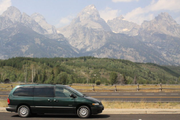 A green minivan in front of a mountain range.