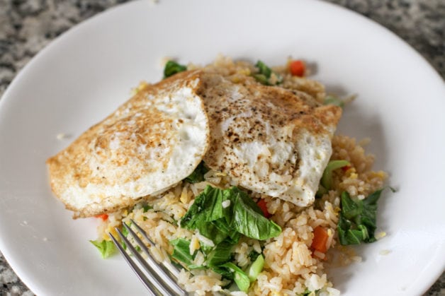 a plate of fried rice with bok choy and eggs.