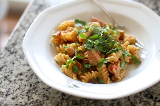 rotini and kielbasa topped with parsley, in a white bowl.