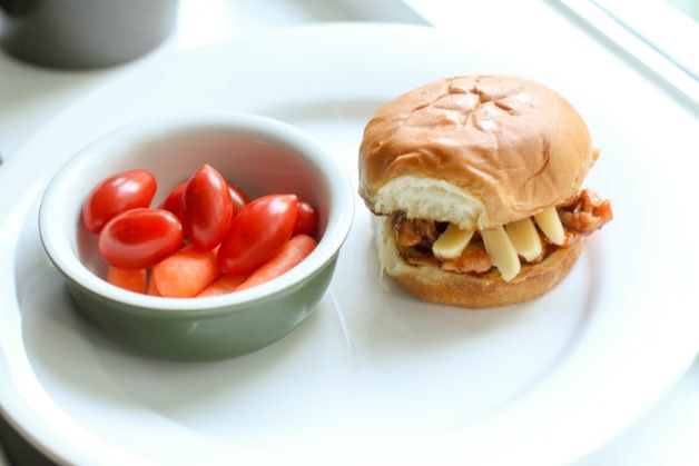 BBQ sandwich on white plate with a bowl of veggies.