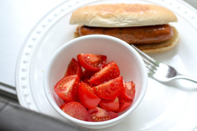 A bowl of tomatoes plus a bratwurst in a bun.