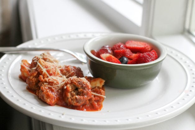 sausage meatballs with a fruit salad on a white plate.