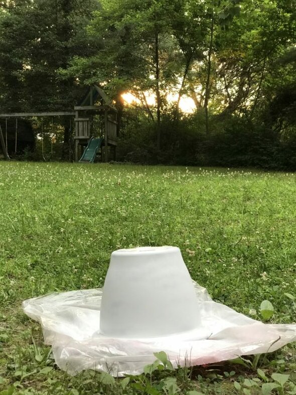 White plant pot sitting on plastic in a yard.