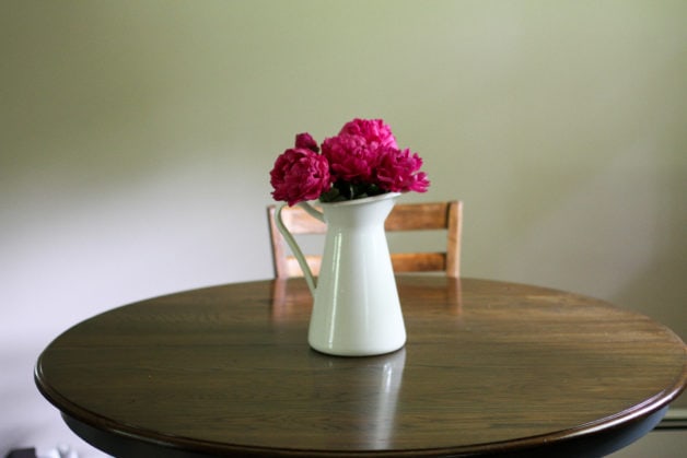 Round table with a vase of pink peonies on top.