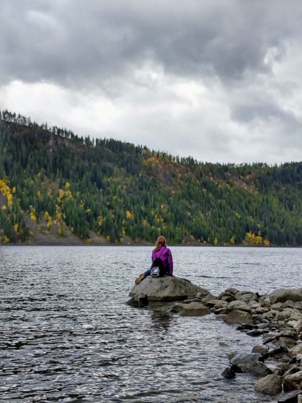 person sitting on a rock in a lake.