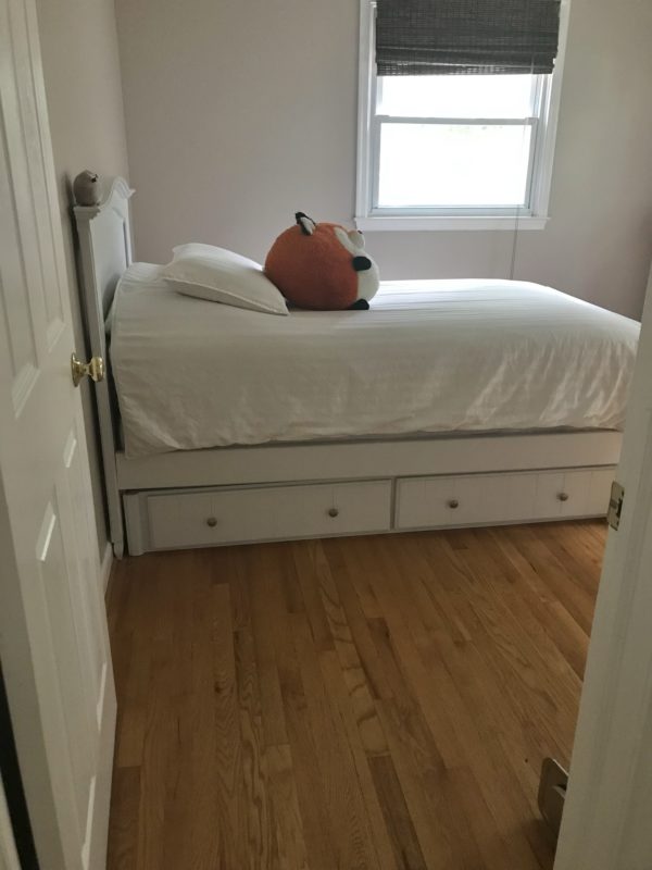 A white bed with a stuffed fox sitting on it.