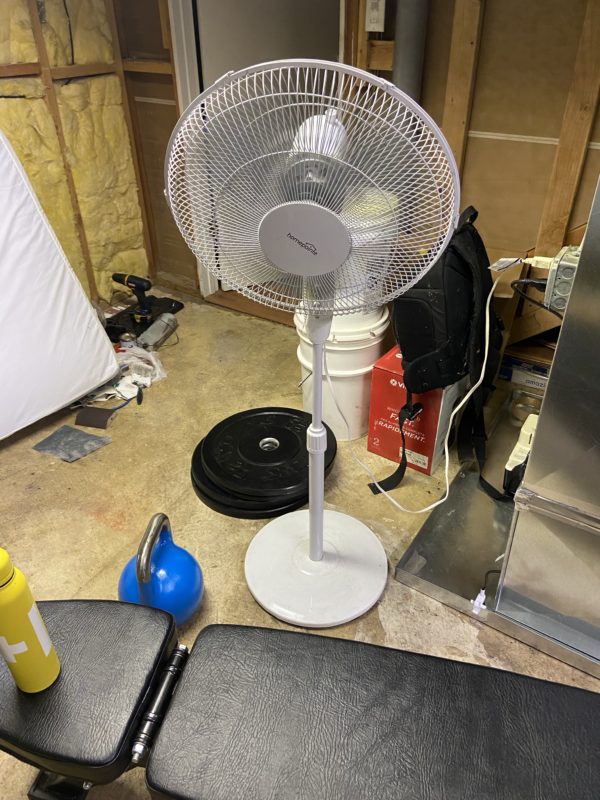 a white floor fan next to a weight bench.