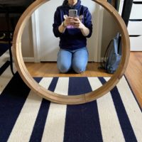 A round mirror with Kristen reflected in it.