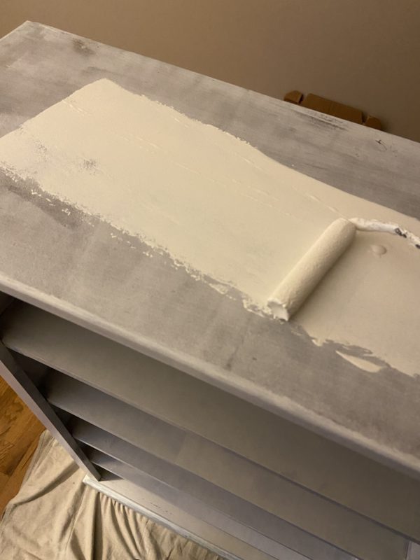 white paint being rolled on top of a bookshelf.