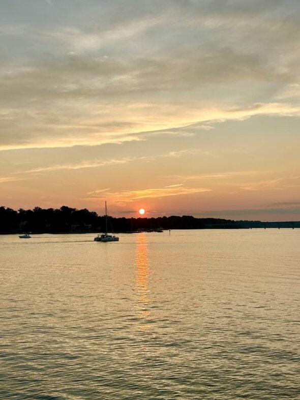 sunset on a river with a boat driving by.